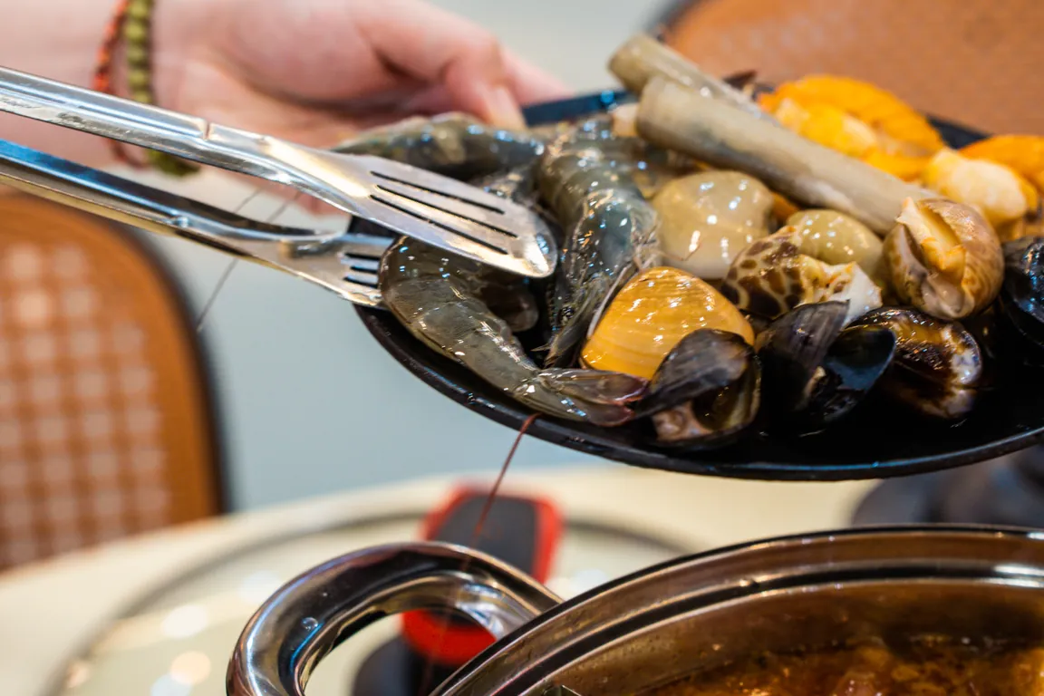 Pinggan makanan laut dipegang di atas periuk steamboat di QQ JB